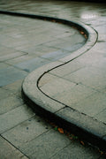 Curved sidewalk with water on wet pavement, evoking subtle leadership, calm orientation, and movement shaped by changing terrain.
