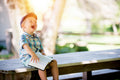 Child sitting on a wooden bench outdoors, holding a book and laughing.