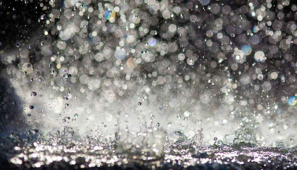 close‑up of fresh may rain with bright droplets bouncing off a surface, capturing the lively, refreshing movement of spring rain and the soft clarity it brings.