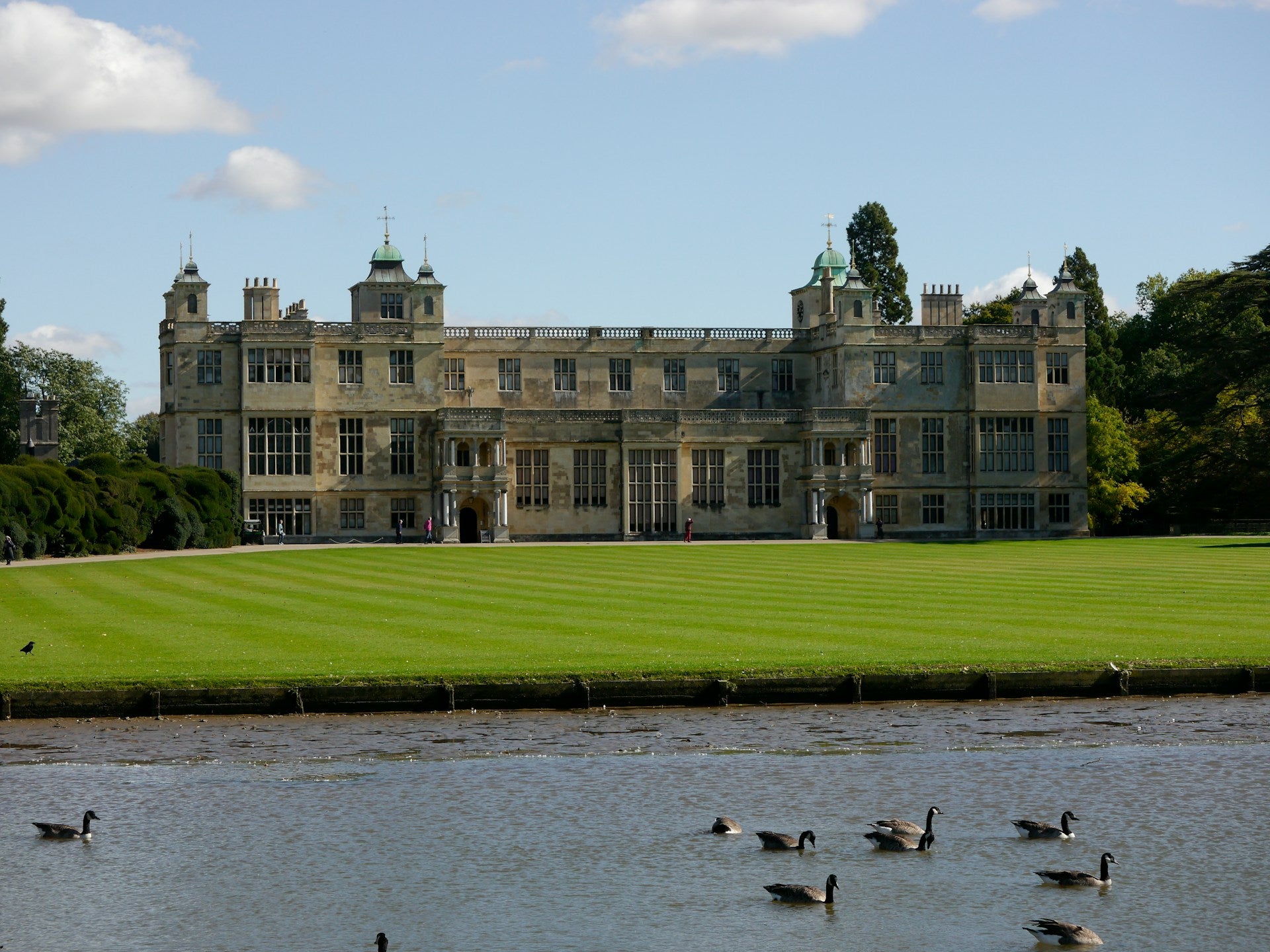 Large historic estate with a pond and wild geese in the foreground — a calm symbol of inner structure, collective wisdom, and reflective inner leadership.