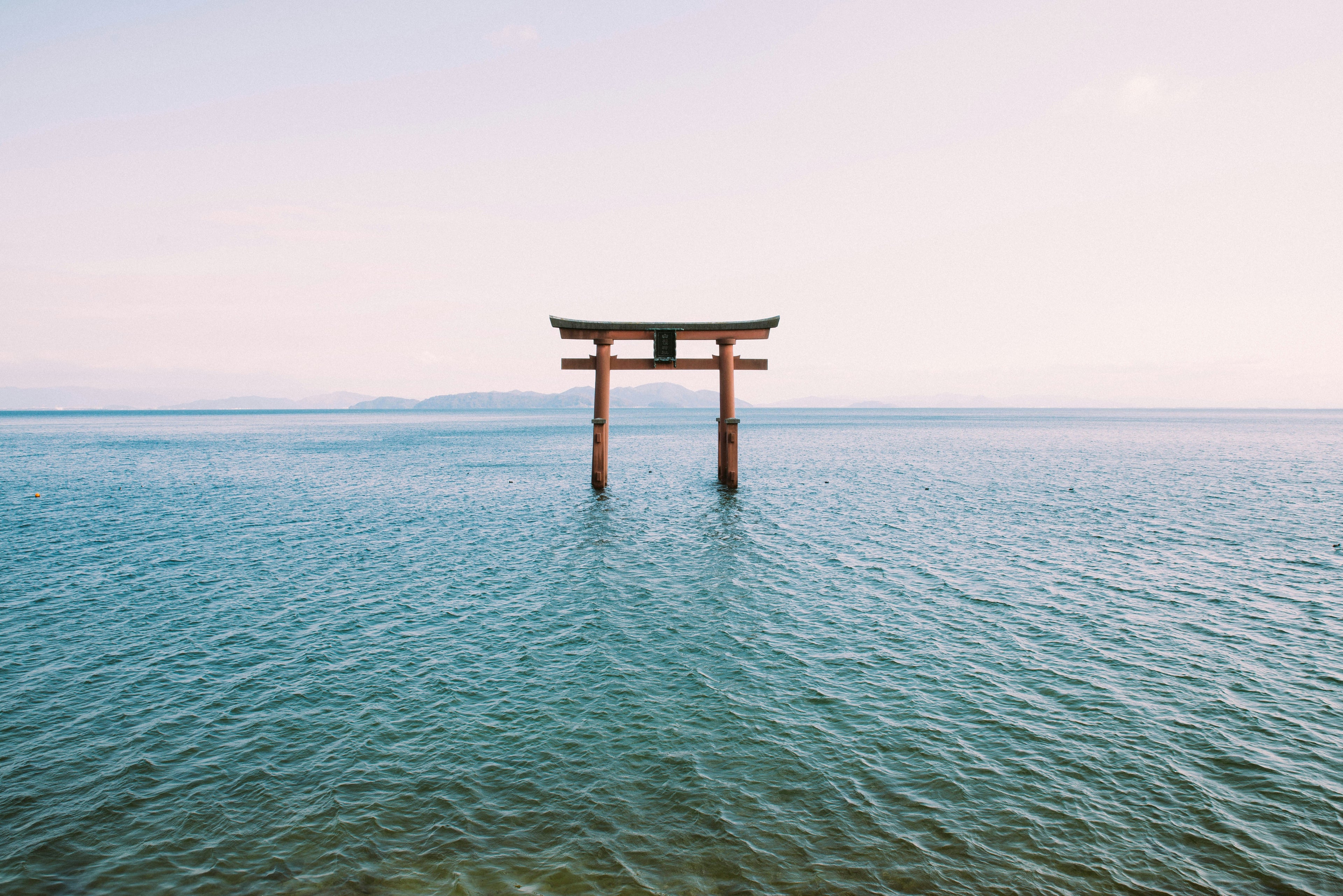 a lone torii gate standing in calm water, appearing to float between worlds — a quiet threshold where the outer world softens and the inner world opens, symbolizing purification, transition, and the soul’s return to its own sacred center.