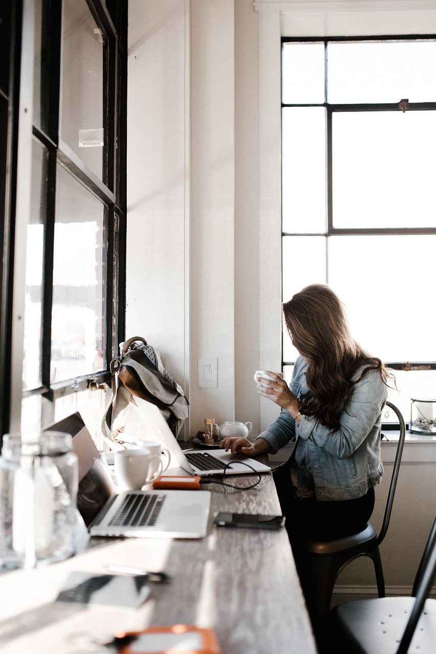 Person sitting at a desk with two laptops and a coffee cup in a bright room — a calm symbol of modern focus, autonomy, and quiet professional clarity.